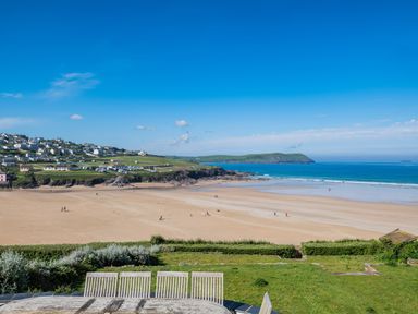A beach with sand and people walking near the ocean with houses on a hill at Treverden in Polzeath