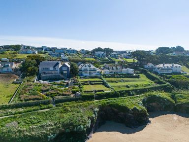 A coastal residential area with houses and terraced gardens overlooking a sandy beach at Treverden in Polzeath