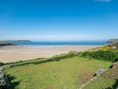 A green lawn overlooking a sandy beach and ocean with hills in the distance at Treverden in Polzeath