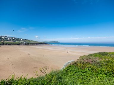 A wide sandy beach with a few people walking near the water and houses on a hill in the distance at Treverden in Polzeath