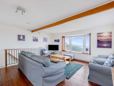 A sitting room with grey sofas a wooden coffee table a blue rug and a large window at Shilling Stones in Port Isaac