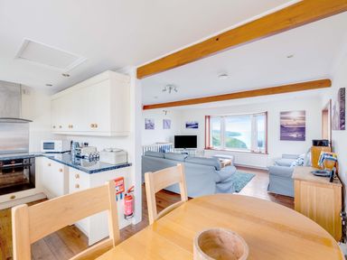 A kitchen with white cabinets and blue countertops next to a living room with blue sofas and a large window with a view at Shilling Stones in Port Isaac
