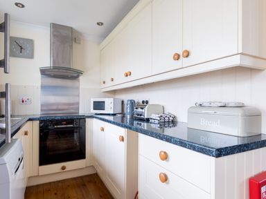 A kitchen with cream cabinets a black oven a microwave kettle toaster bread box and blue countertop at Shilling Stones in Port Isaac