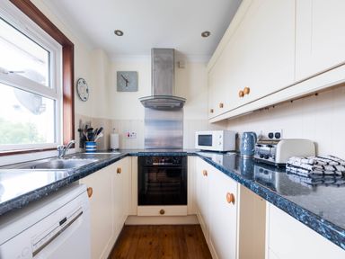 A kitchen with white cabinets wooden knobs a dishwasher a microwave a kettle a toaster and a sink at Shilling Stones in Port Isaac
