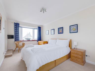 A bedroom with a double bed white bedding wooden furniture and blue curtains at Shilling Stones in Port Isaac