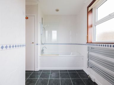 A bathroom with a bathtub shower combination a tiled floor and a wall-mounted radiator at Shilling Stones in Port Isaac