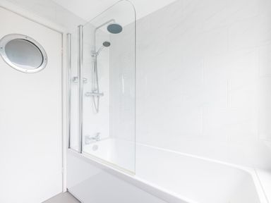 A bathtub with a wall-mounted showerhead and a glass shower screen in a bathroom at Shilling Stones in Port Isaac