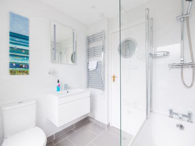 A bathroom with a toilet sink mirror towel rack shower and blue wall art at Shilling Stones in Port Isaac