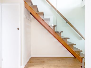 A staircase with wooden steps and glass railing in a room with wooden floor and white walls at Shilling Stones in Port Isaac