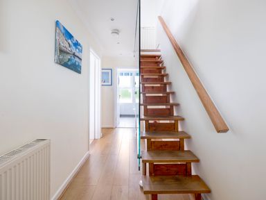 A hallway with wooden stairs on the right and doors leading to other rooms at Shilling Stones in Port Isaac