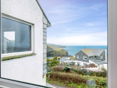 A coastal view through a window showing white buildings with slate roofs bushes and the sea at Shilling Stones in Port Isaac