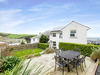 An outdoor patio with metal table and chairs next to a white house with solar panels and garden at Shilling Stones in Port Isaac