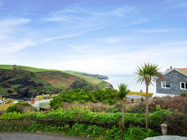 A coastal landscape with grassy hills shrubs and houses overlooking the sea at Shilling Stones in Port Isaac