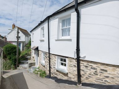 A white cottage with stone lower walls and black drainpipes beside a narrow street at Bre Cottage in Port Isaac