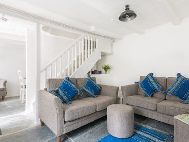 A living room with two grey sofas and blue cushions near a staircase at Bre Cottage in Port Isaac