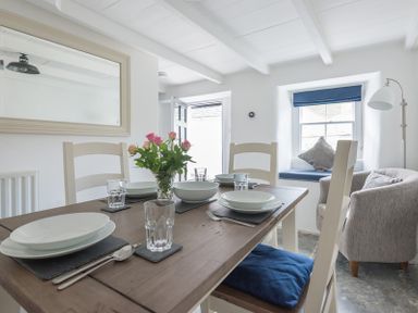 A dining area with set table with plates glasses and cutlery and a window seat with cushions at Bre Cottage in Port Isaac