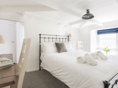 A bedroom with a bed with white linens and rolled towels a desk with books and a window with blue blind at Bre Cottage Port Isaac