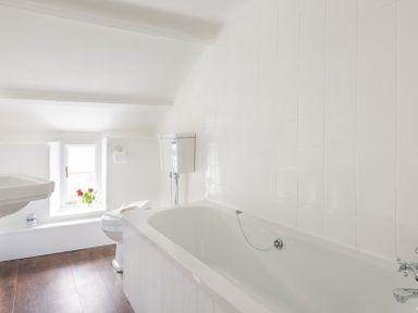 A bathroom with a bathtub sink toilet and a window with flowers at Bre Cottage in Port Isaac