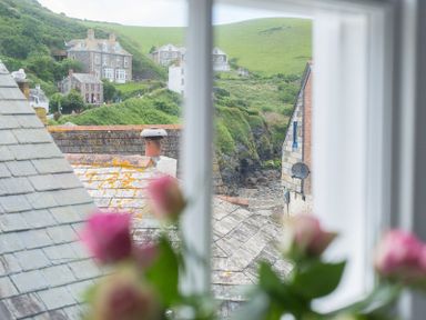 A window view showing rooftops and houses with green hills in the background at Bre Cottage in Port Isaac