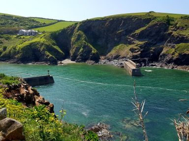 A coastal landscape with green hills rocky cliffs and a concrete pier at Bre Cottage in Port Isaac