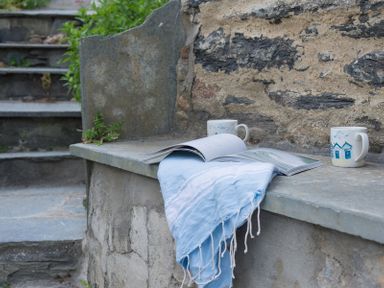 A stone bench with a blue cloth two mugs and an open book next to stone steps at Bre Cottage in Port Isaac