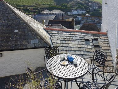 A balcony with a round metal table and four chairs set with a teapot cups and biscuits overlooking rooftops at Bre Cottage in Port Isaac