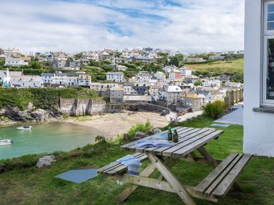 A picnic table with bottles and a magazine on the grass overlooking a harbor and village at Folly 2 in Port Isaac