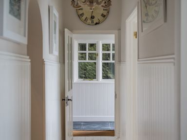 A hallway with doors and a window at the end under a wall clock at Folly 2 in Port Isaac