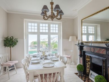 A dining room with a white table set for six by a window overlooking water and cliffs at Folly 2 in Port Isaac