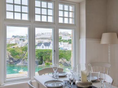 A dining table with plates glasses and a candle near a window with a view of houses and a body of water at Folly 2 in Port Isaac