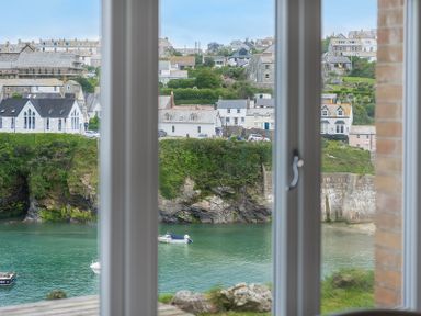 A view through a window of boats on water and houses on a hillside at Folly 2 in Port Isaac