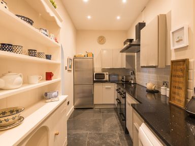A kitchen with shelves holding cups and bowls and a counter with a stove and refrigerator at Folly 2 in Port Isaac