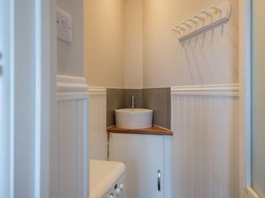 A small bathroom with a round sink on a wooden countertop a white cabinet below and a washing machine on the left at Folly 2 in Port Isaac