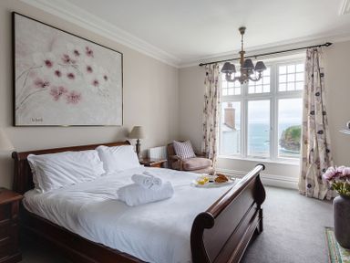 A bedroom with a wooden bed and white linens next to a window with floral curtains at Folly 2 in Port Isaac