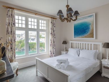 A bedroom with a white bed and nightstands beside a window with curtains at Folly 2 in Port Isaac