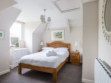 A bedroom with a wooden bed and white bedding with bedside tables lamps and a window at Folly 2 in Port Isaac