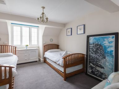 A bedroom with two single wooden beds a white dresser under a window and framed artwork on the walls at Folly 2 in Port Isaac