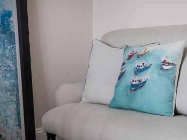 A sofa with two cushions one with a boat pattern next to a blue and white painting at Folly 2 in Port Isaac