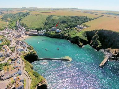 A coastal village with houses fields cliffs a bay with boats and two piers at Folly 2 in Port Isaac