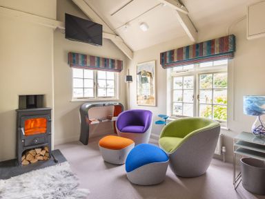 A living room with colorful chairs and a small stove at Crow's Nest in Port Isaac