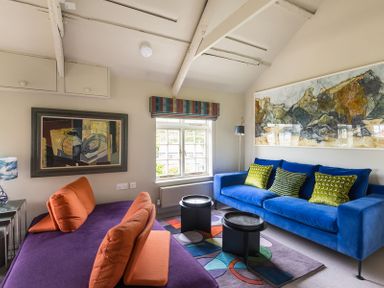 A living room with a blue sofa and orange cushions next to a purple sofa and colorful rug at Crow's Nest in Port Isaac