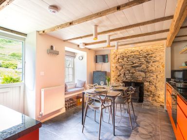 A kitchen and dining area with a stone wall fireplace and orange cabinets at Crow's Nest in Port Isaac