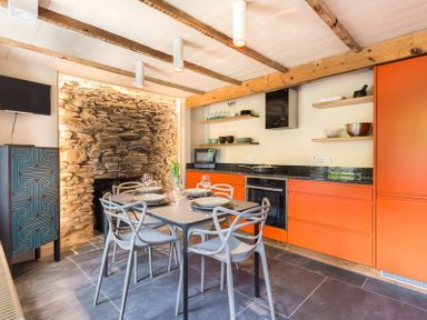 A kitchen dining area with orange cabinets stone wall and a table set with plates and glasses at Crow's Nest in Port Isaac