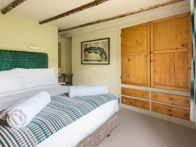 A bedroom with a bed with rolled towels on a patterned blanket wooden built-in wardrobe and a framed picture on the wall at Crow's Nest in Port Isaac