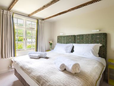 A bedroom with a double bed with white pillows and rolled towels and a window with curtains at Crow's Nest in Port Isaac