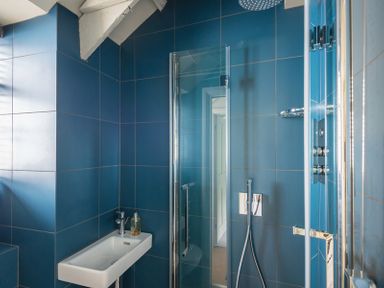 A bathroom with blue tiled walls a white sink with a faucet a glass shower door and a showerhead at Crow's Nest in Port Isaac
