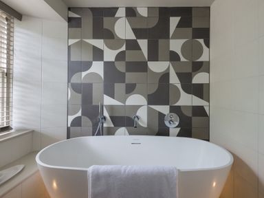 A bathroom with a white freestanding bathtub and geometric patterned tiles on the wall at Crow's Nest in Port Isaac