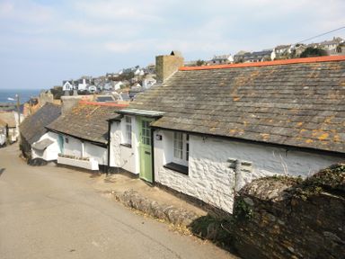 A stone house with a green door on a sloped street near the coast at Crow's Nest in Port Isaac
