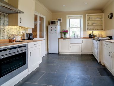 A kitchen with white cabinets a refrigerator a microwave a window a countertop with appliances and flowers at Worthy House Daymer Bay