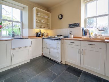 A kitchen with white cabinets a farmhouse sink a white cooker and countertop appliances at Worthy House in Daymer Bay
